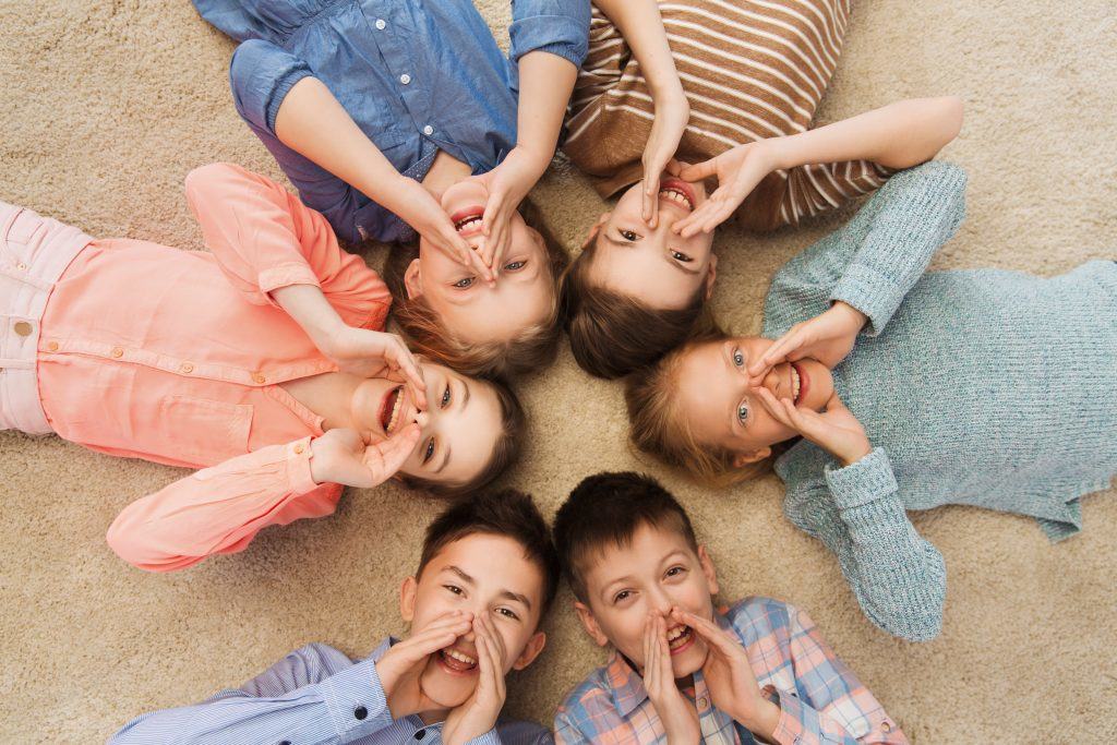 childhood, fashion, friendship and people concept - happy smiling children lying on floor in circle and calling or shouting